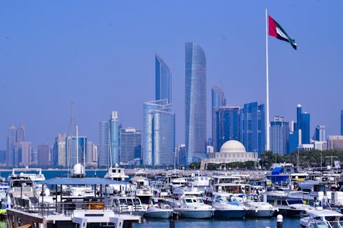 A scenic view of Abu Dhabi marina with July 2025 Astrology Forecastmodern skyscrapers and a flag in the foreground.
