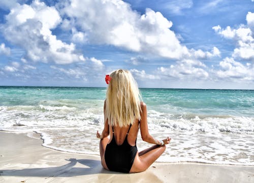 July 2025 Astrology ForecastA woman meditates on a beautiful tropical beach in the Bahamas, under a clear blue sky.