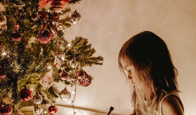December 2025 Horoscope: Closing the Cycle 9 & Numerology ForecastA young girl writes in a notebook by a Christmas tree adorned with decorations and lights.