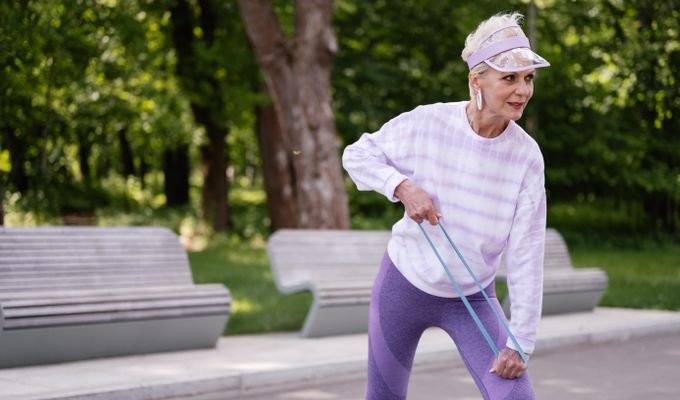 4 Healthy Aging Tips for Older AdultsSenior woman performing outdoor exercise with a resistance band in a park setting.