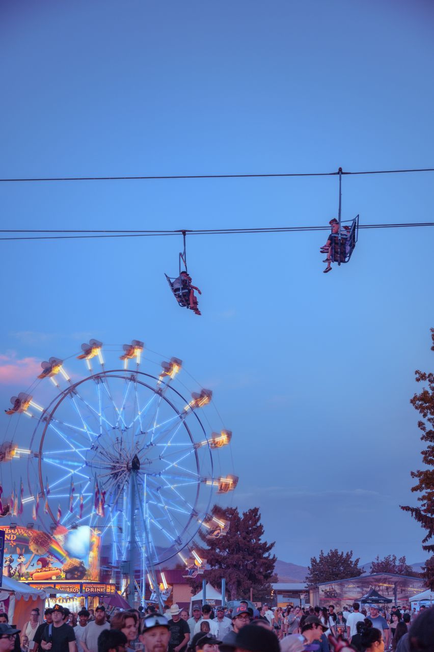July 2026 Monthly Horoscope: Capturing the lively atmosphere of an evening amusement park with a glowing Ferris wheel and zipline riders.