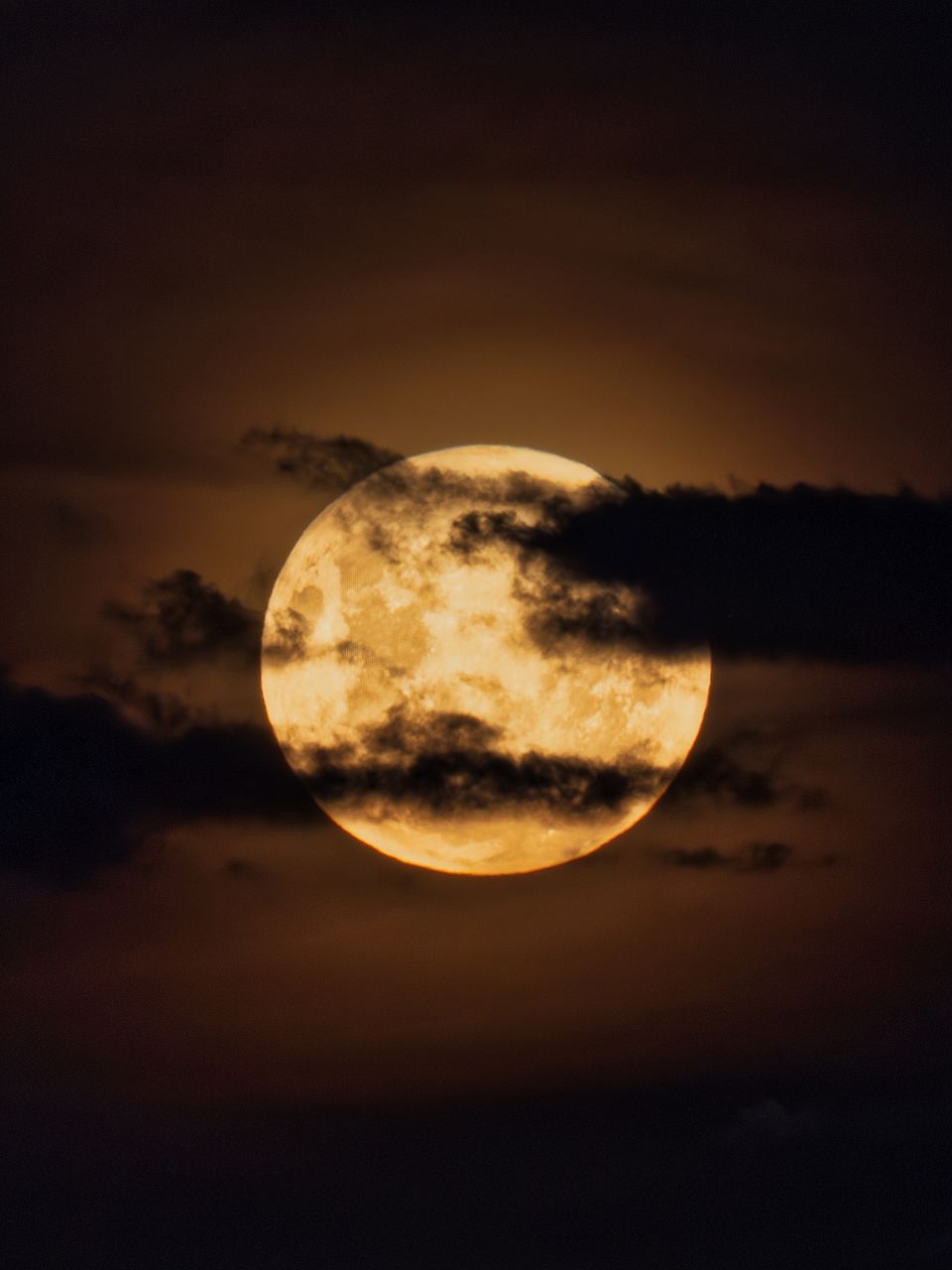 Captivating full moon in a dramatic night sky partially obscured by clouds, creating a moody atmosphere.