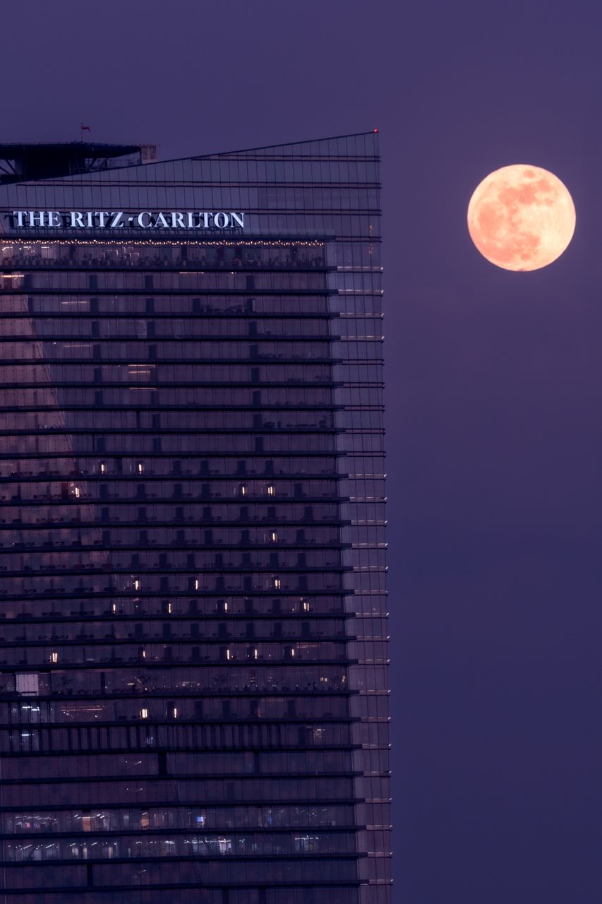 Captivating night view of The Ritz-Carlton skyscraper with a full moon in the sky.